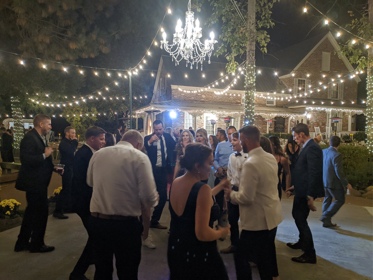 Guests dance beneath the crystal chandelier and string lights in front of the brick lodge