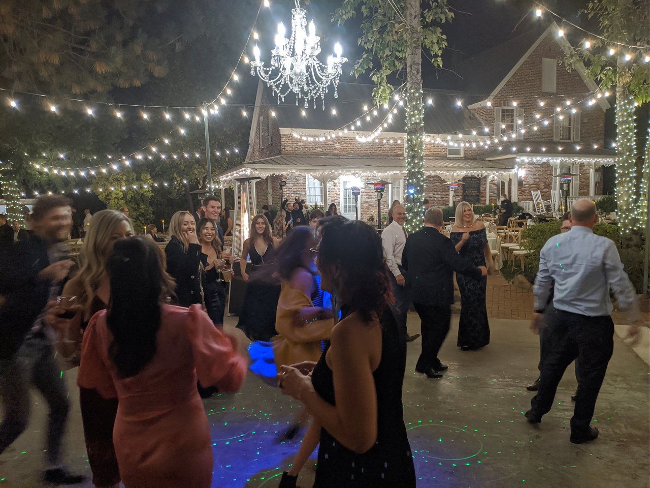 Guests dance under the crystal chandelier and string lights in front of the brick house
