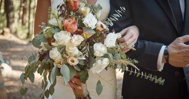 Nicole's bouquet of white roses, peach blooms and eucalyptus beside a man in a dark suit