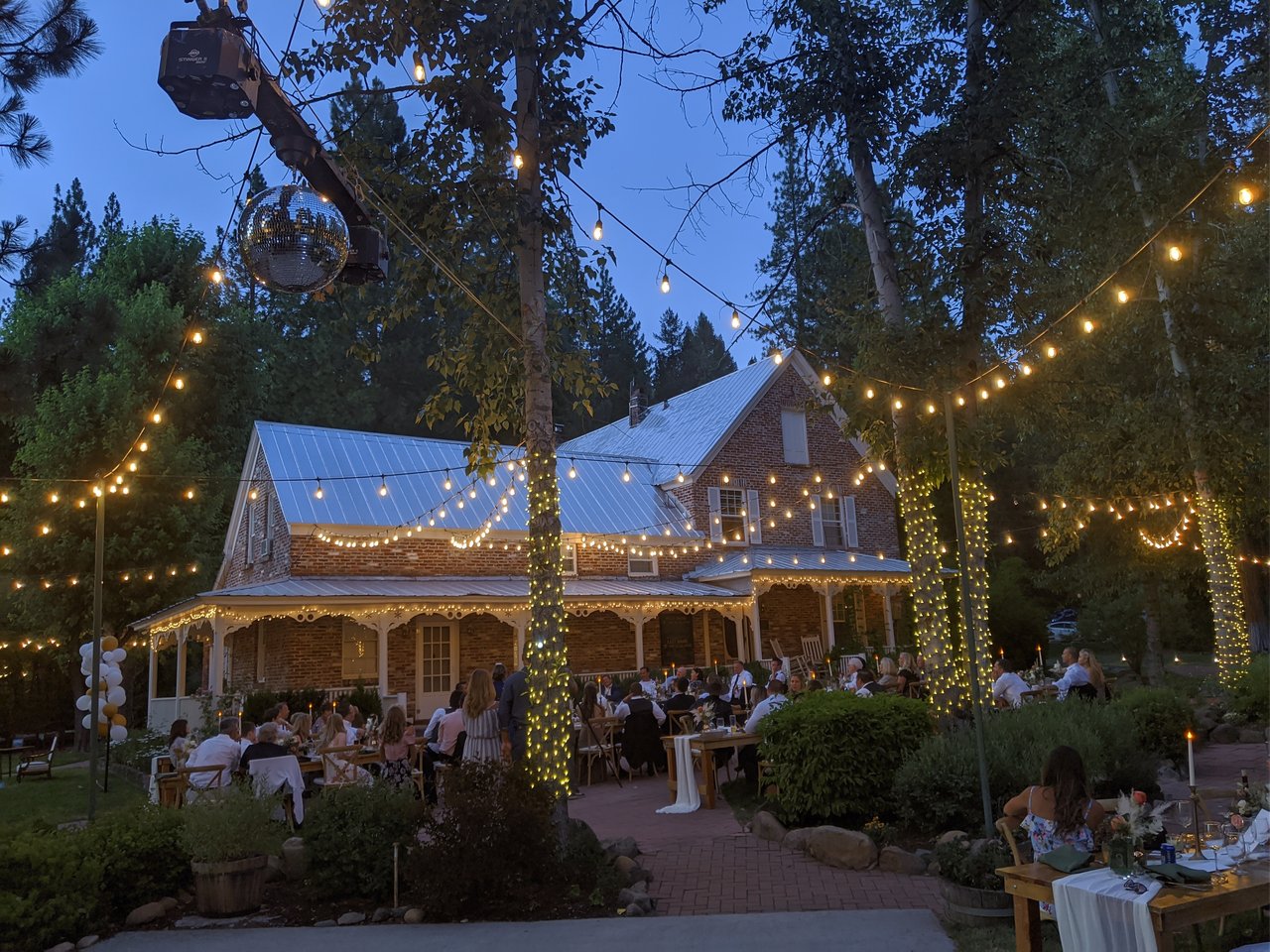 Guests at long candlelit tables on the brick patio under string lights at dusk