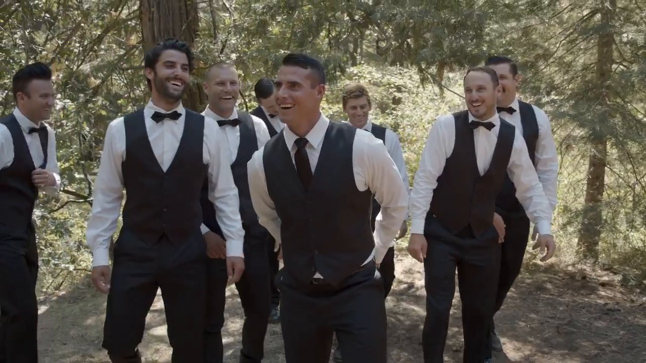 Tim and his groomsmen laugh in the trees in black vests and bow ties.
