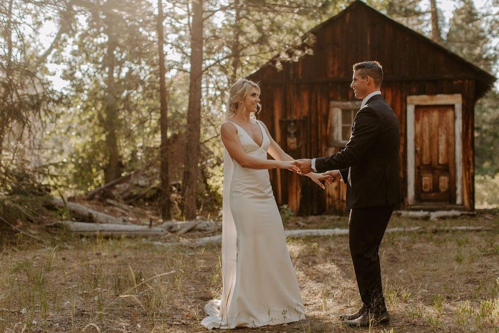 Nicole and Tim hold hands in front of the old wooden cabin, photo by Taylor McCutchan Photography
