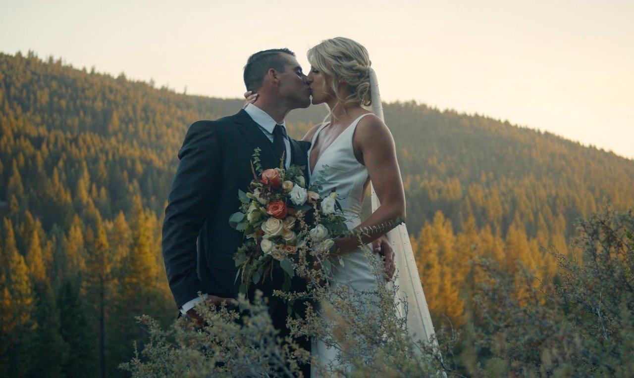 Nicole and Tim kiss on a ridge above the forest in the warm light of sunset