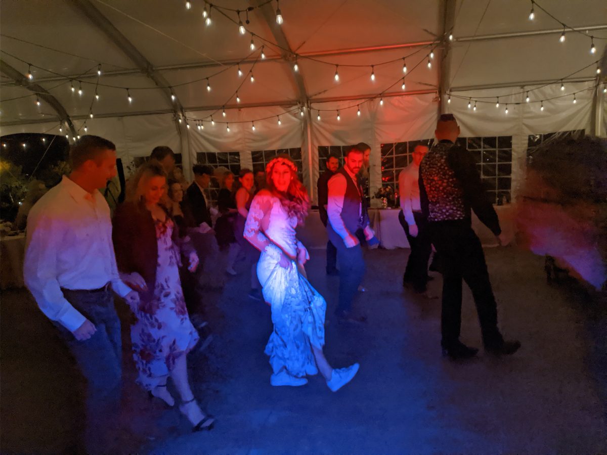 The newlyweds dance surrounded by friends under warm stage lighting at Sunridge