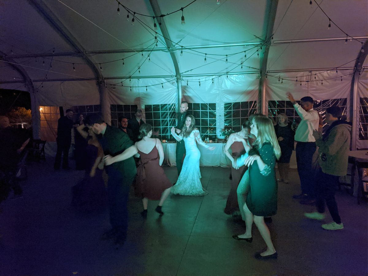The bride dances with guests under teal light at Rachel and Christopher's Carson City reception