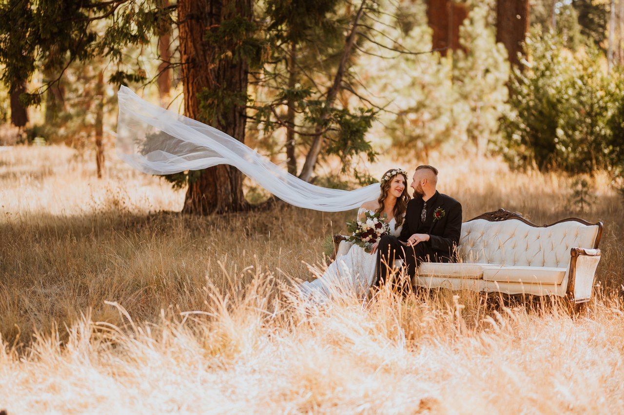 Rachel's veil blows out beside a vintage sofa in the meadow