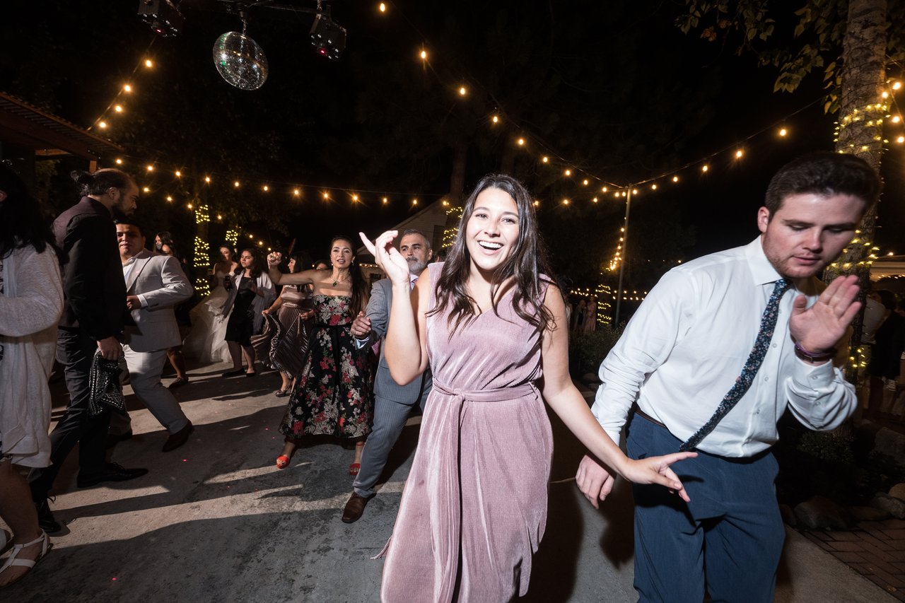 A bridesmaid in blush and a guest dance together under the string lights
