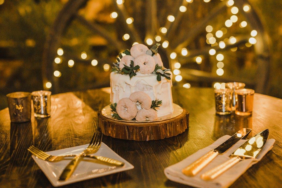 Their donut topped cake on a wood slice with glowing lights behind it, photo by Composing Reality Photography