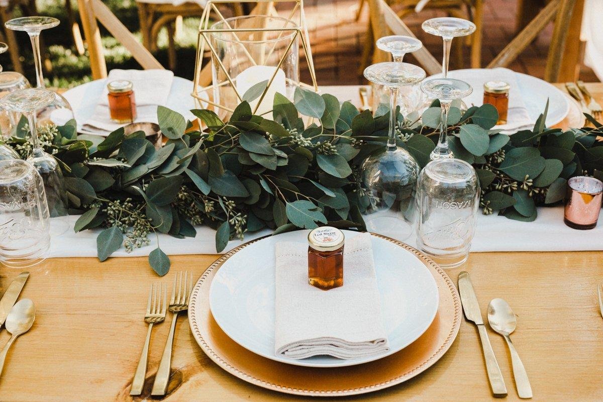 A place setting with a honey jar and a eucalyptus runner on a gold charger, photo by Composing Reality Photography