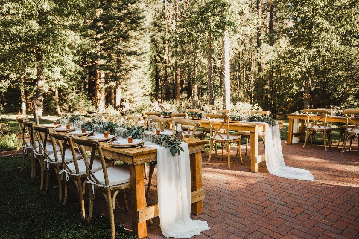 Long wooden tables with white runners set on the brick patio among the pines, photo by Composing Reality Photography